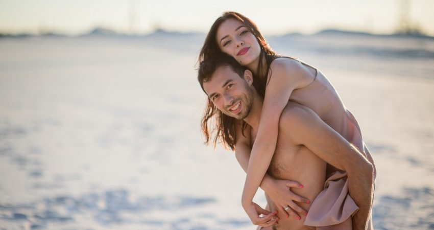 Man holds pretty woman on his back walking on the beach